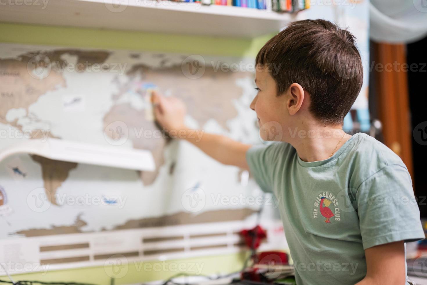Boy shows Ukraine with his finger on the world map in children's room. photo