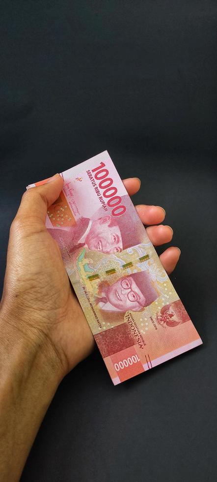 retrato de billetes de banco indonesios rp. 100.000 en mano. moneda rupia indonesia aislado sobre fondo negro foto