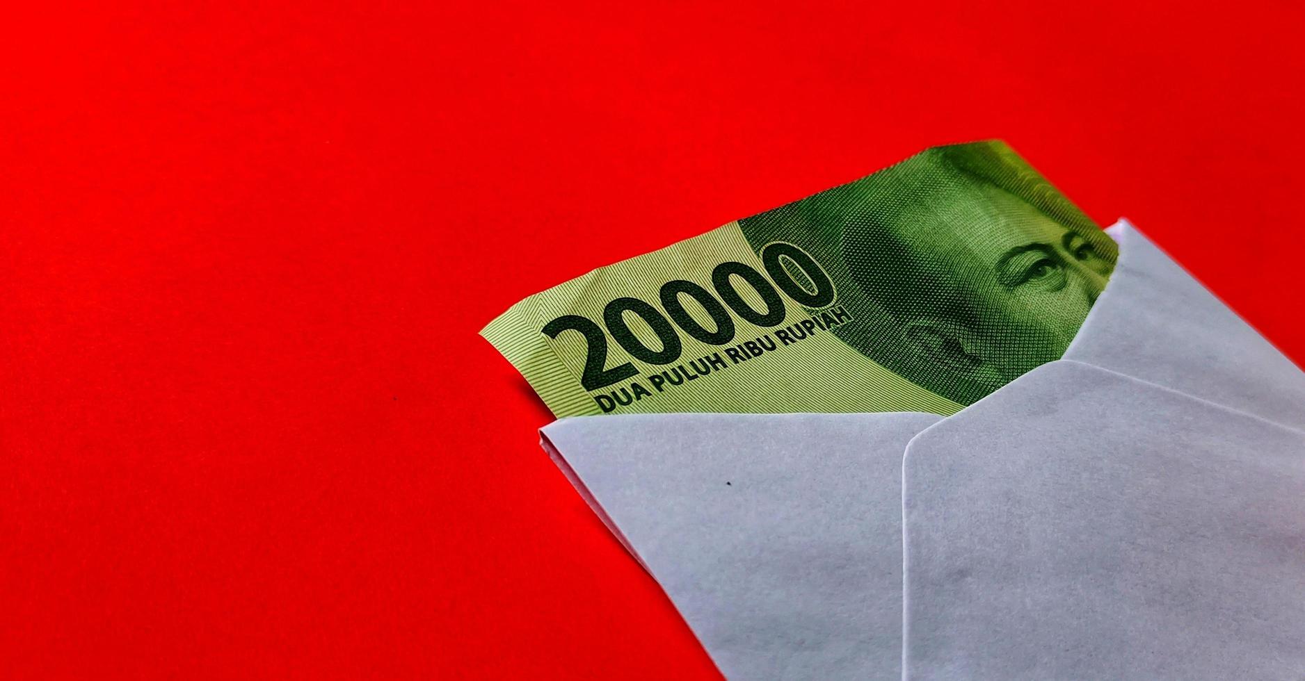 Indonesian rupiah banknotes worth IDR 20,000 in a white envelope isolated on red background photo
