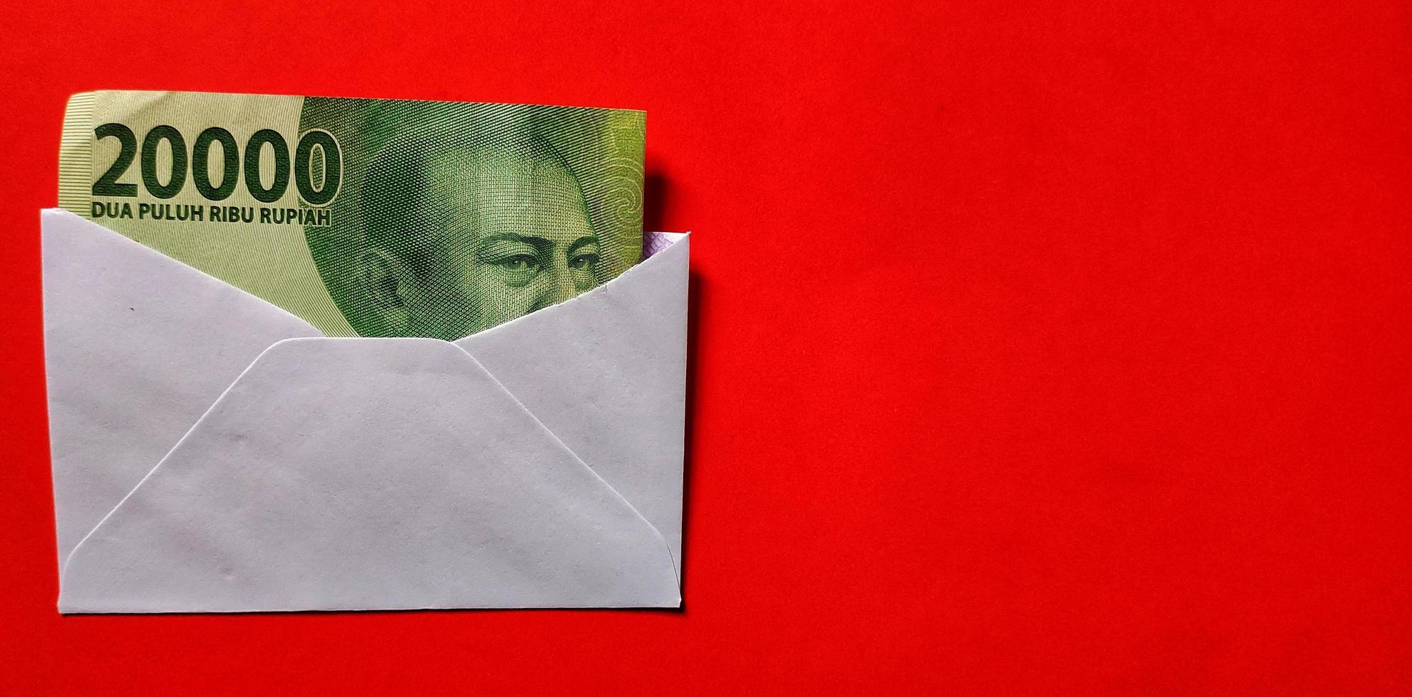 Indonesian rupiah banknotes worth IDR 20,000 in a white envelope isolated on red background photo