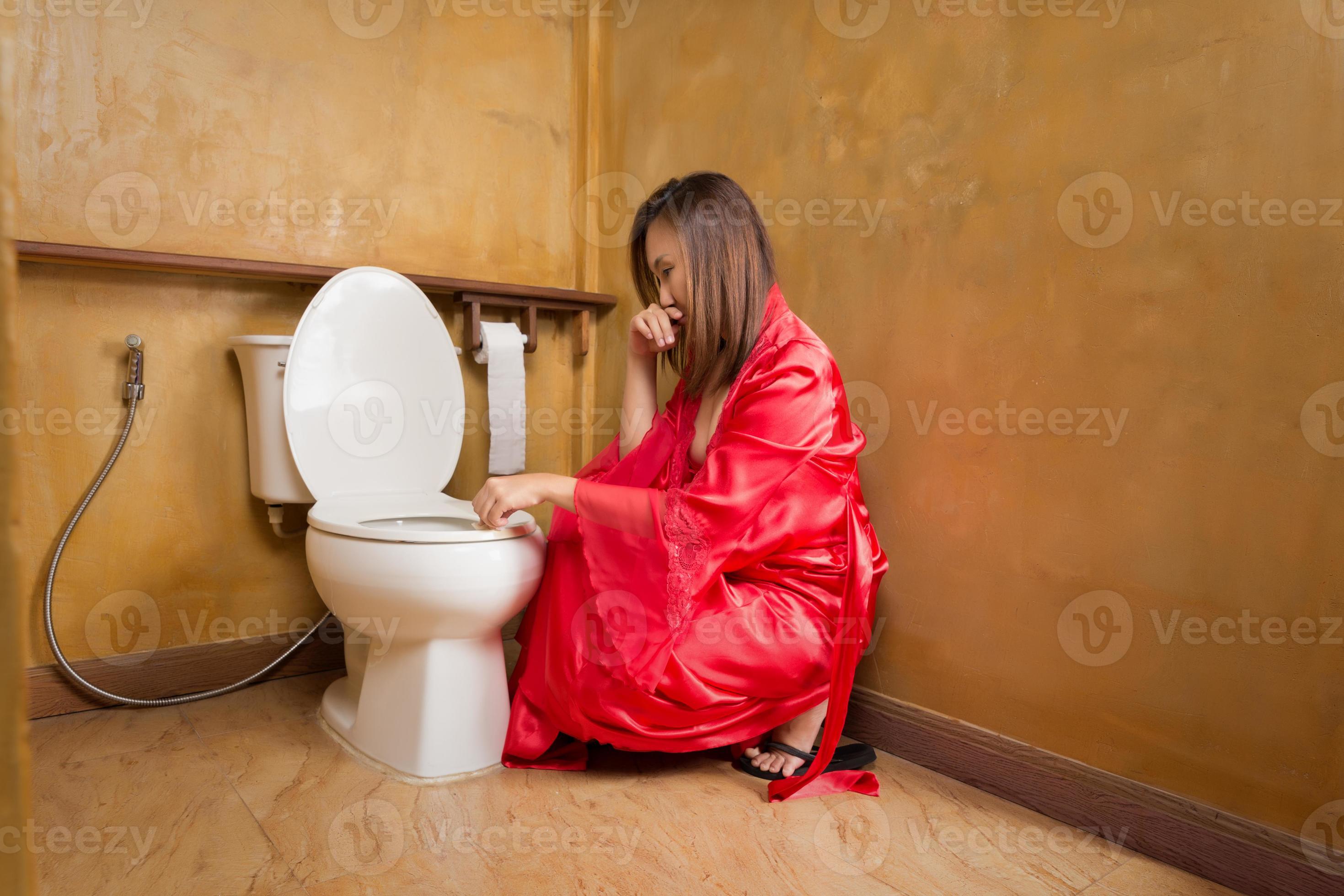 Asian woman in a nightgown and red satin robe wiping the toilet seat at