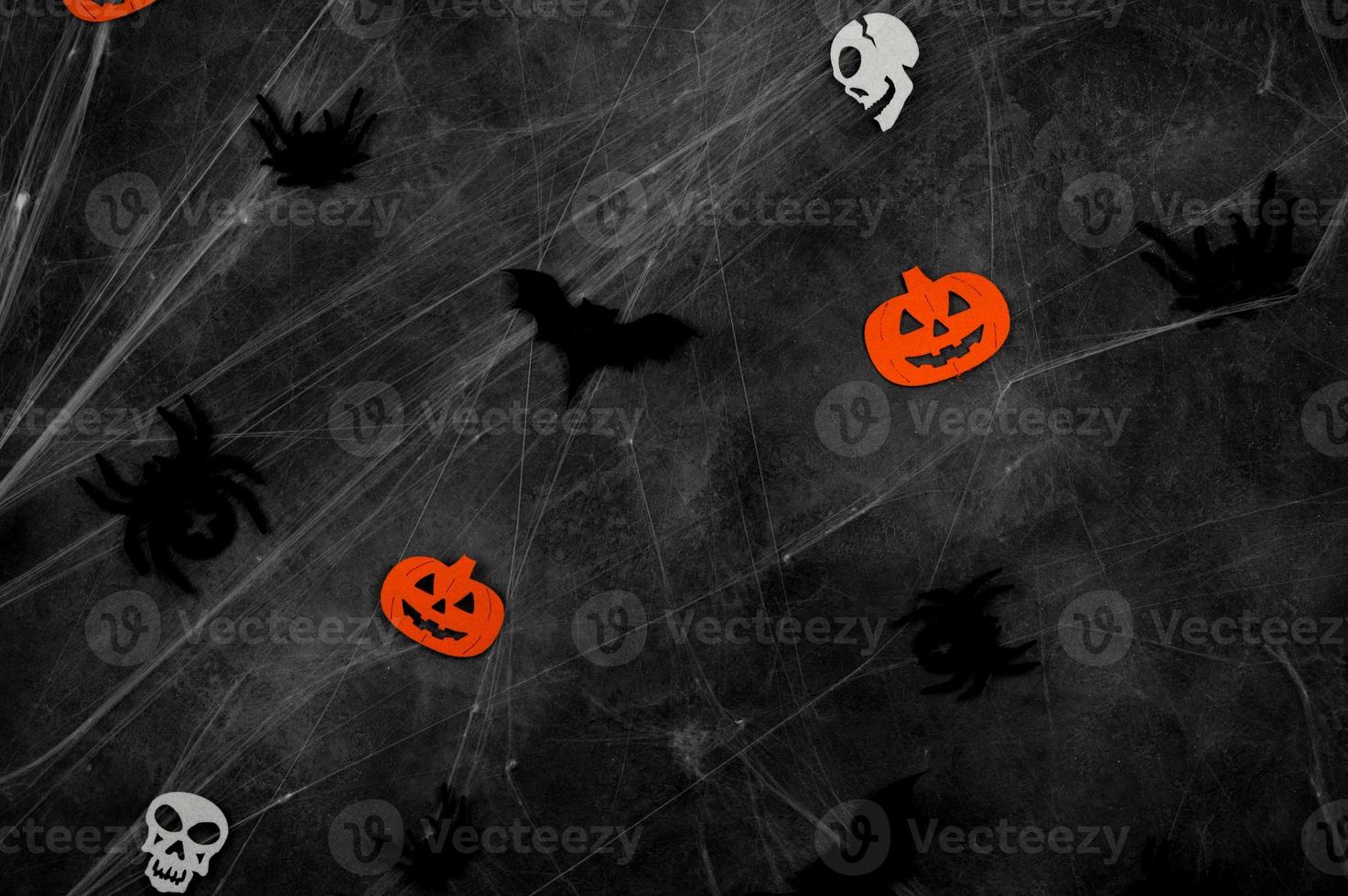 black flying bats, spiders,skulls and pumpkins on web over dark concrete background photo