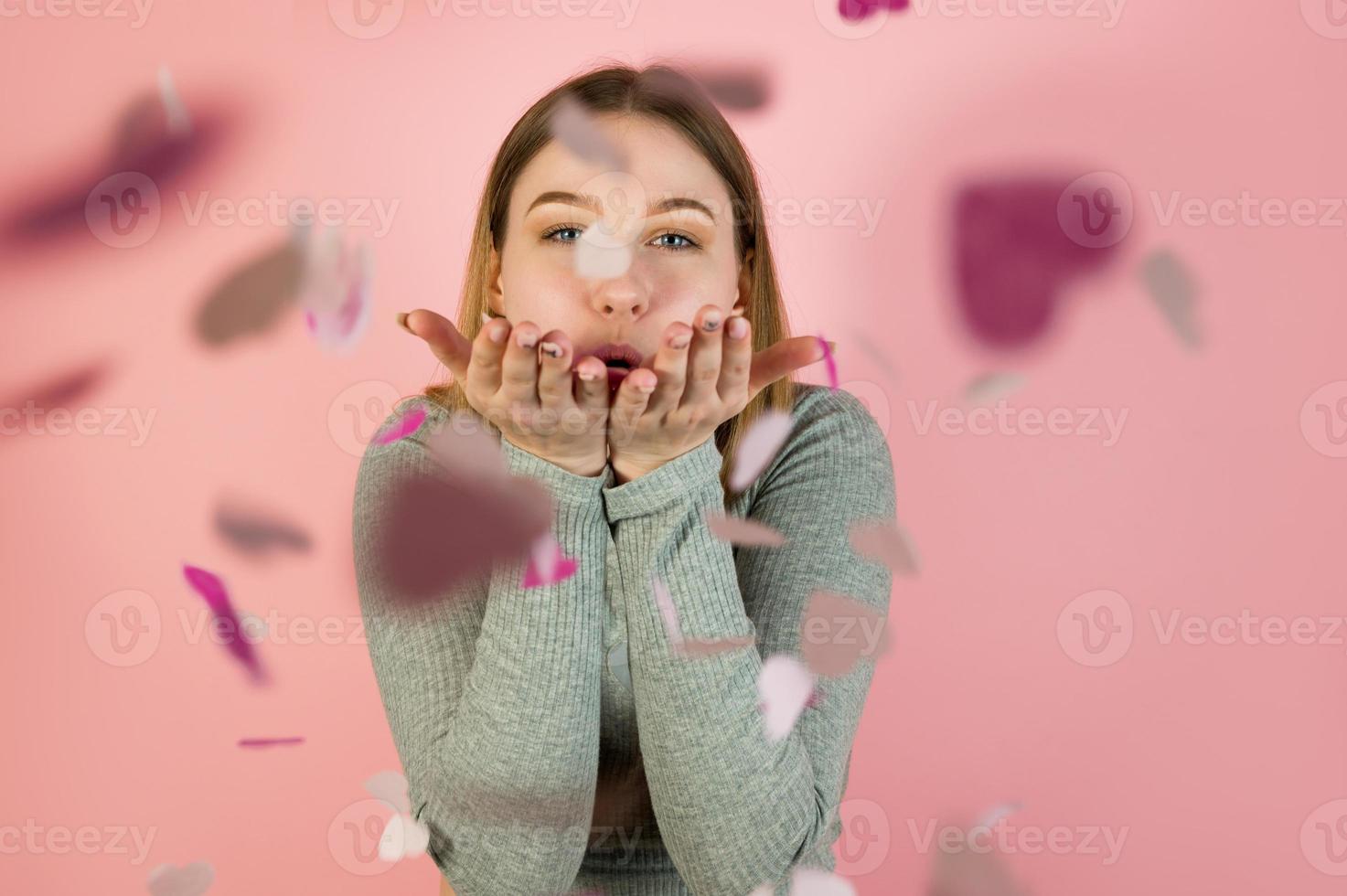 retrato de estudio de una joven mujer feliz que sopla confeti en forma de corazón. concepto del día de san valentín foto