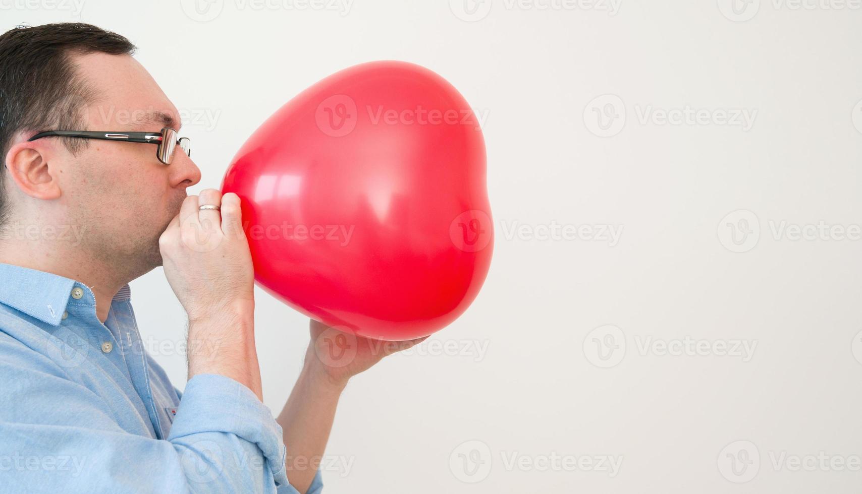 vista lateral de un hombre que sopla un globo de corazón preparándose para el día de san valentín o el aniversario foto