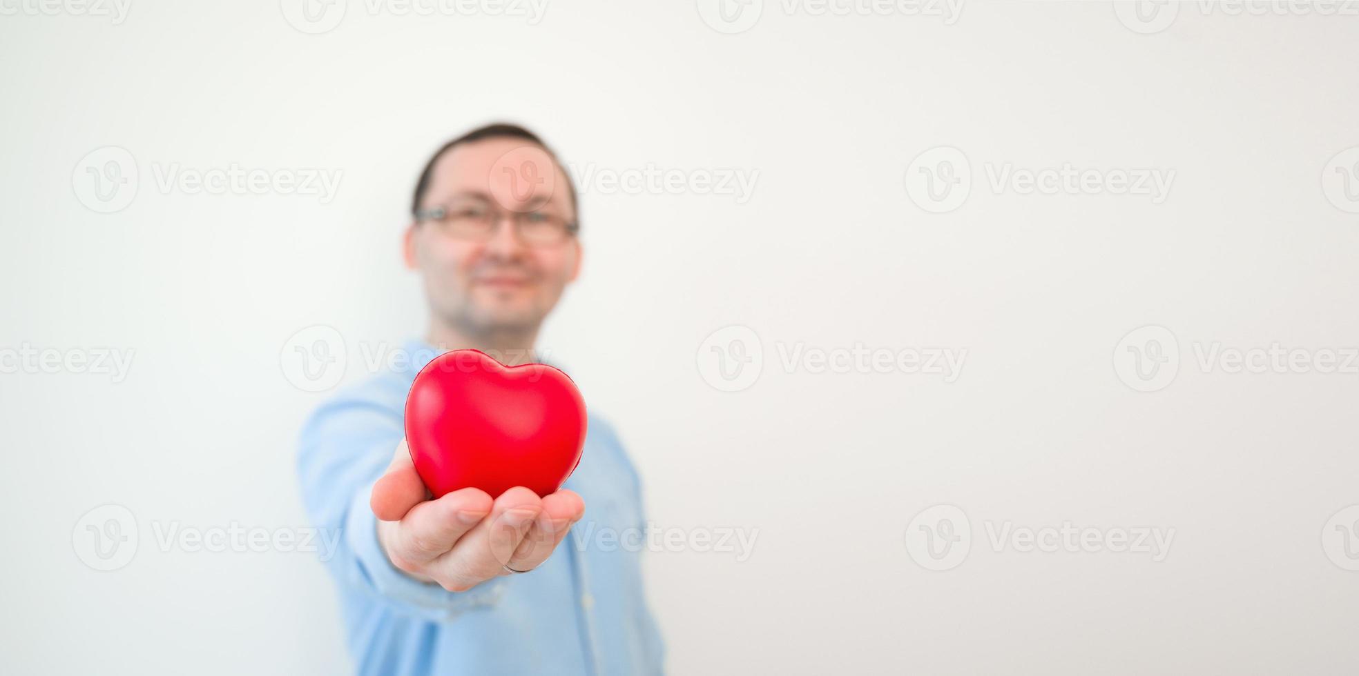 Young smiling man holding heart against white wall. VAlentines banner with place for text photo