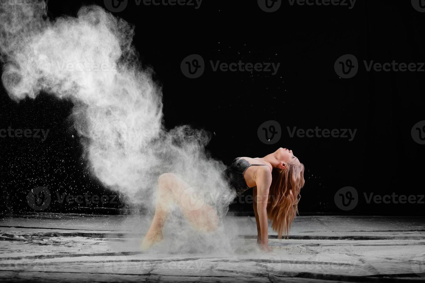 Young beautiful woman with spread flour on the air on a black background photo