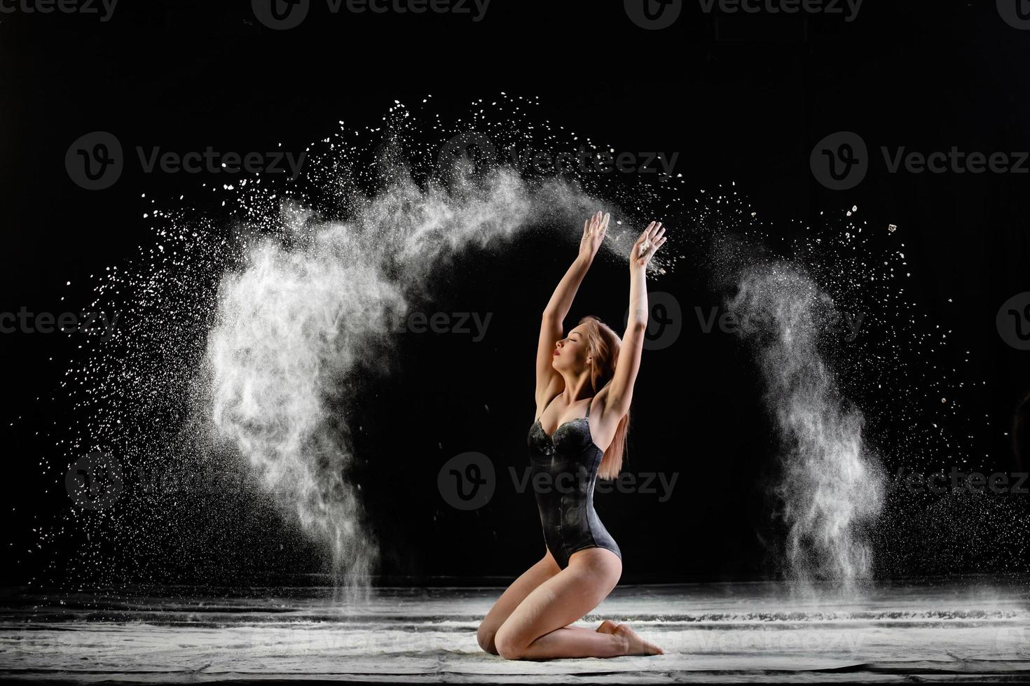 Young beautiful woman with spread flour on the air on a black background photo