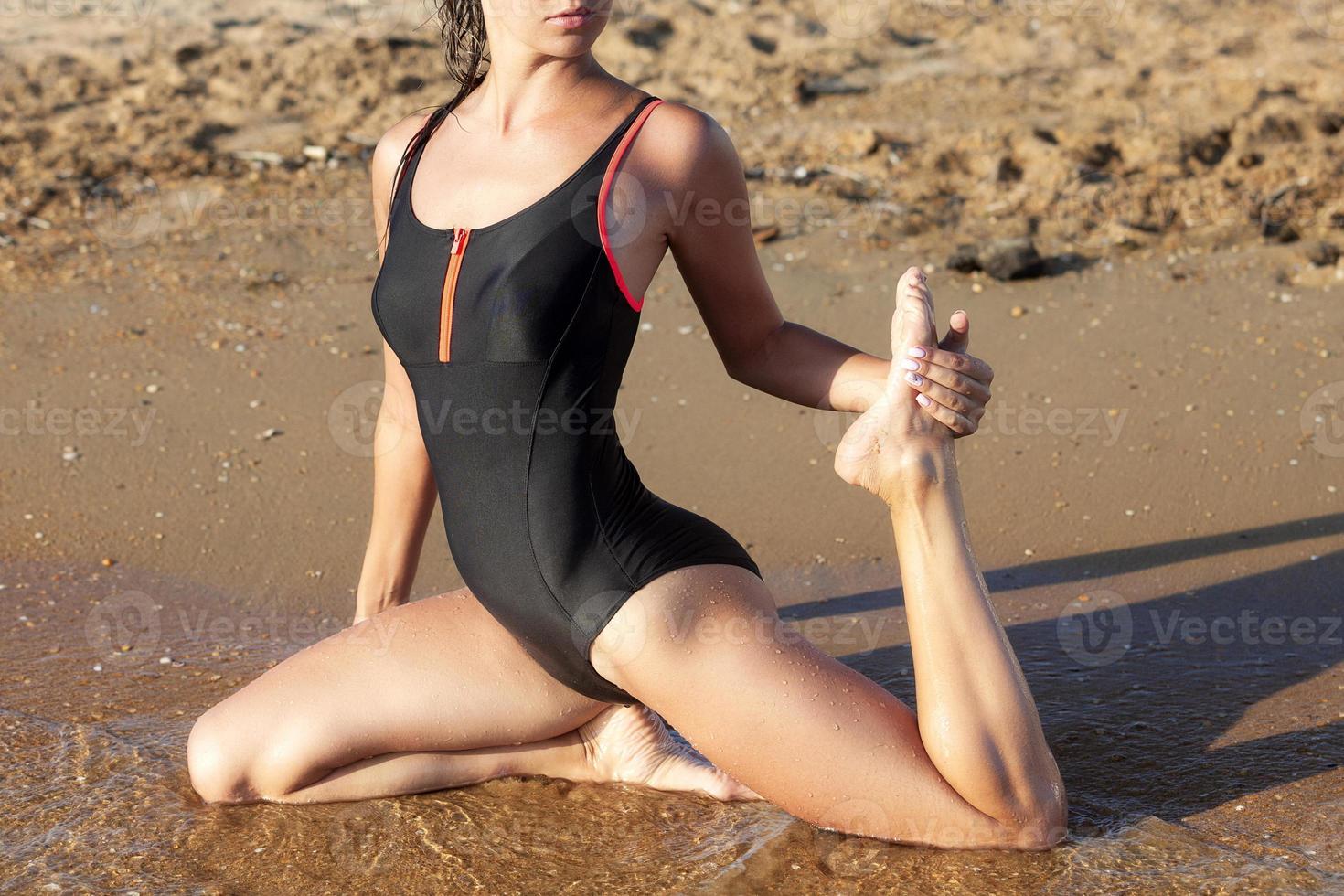 Yoga gymnastics on a beach. Sporty woman in black swimsuit photo