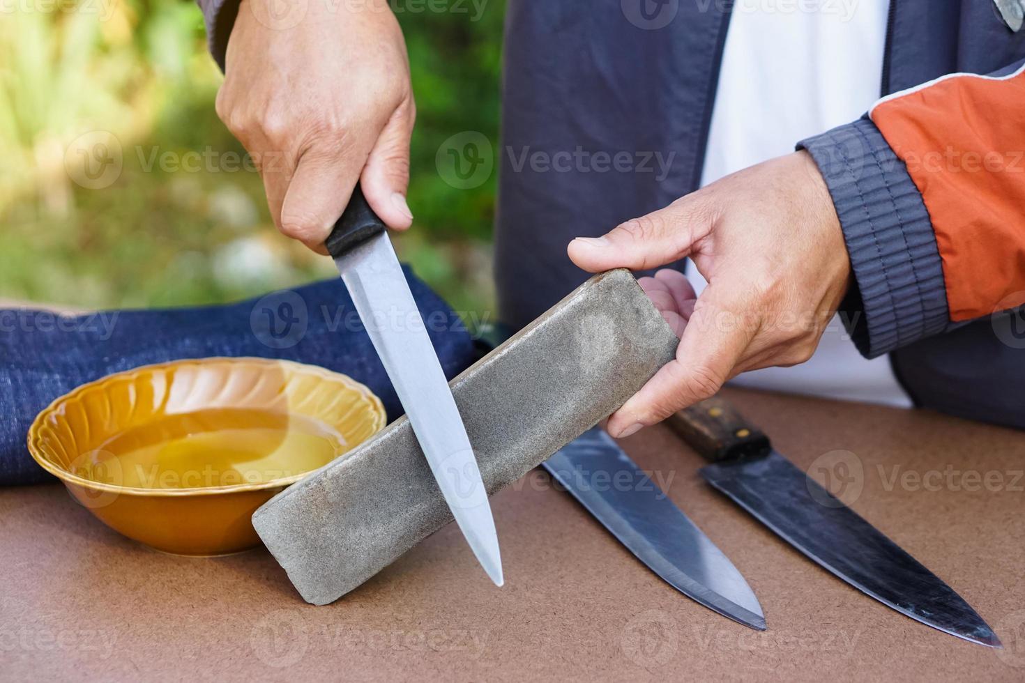 Closeup man hands sharpen knife on whetstone sharpener or grindstone. Concept, maintenance tools for cooking, make knife sharp ,not dull for long live using. Original style. photo