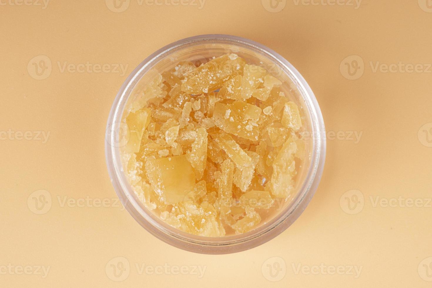 glass jar with golden cannabis wax, pieces of hardened resin of marijuana extract on an orange background photo