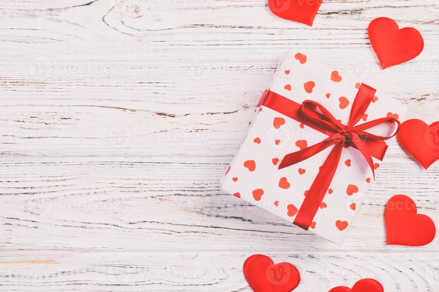 Valentine or other holiday handmade present in paper with red hearts and gifts box in holiday wrapper. Present box of gift on white wooden table top view with copy space, empty space for design photo