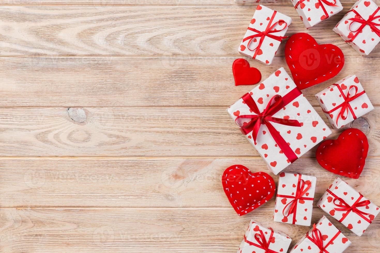 Valentine or other holiday handmade present in paper with red hearts and gifts box in holiday wrapper. Present box of gift on orange wooden table top view with copy space, empty space for design photo