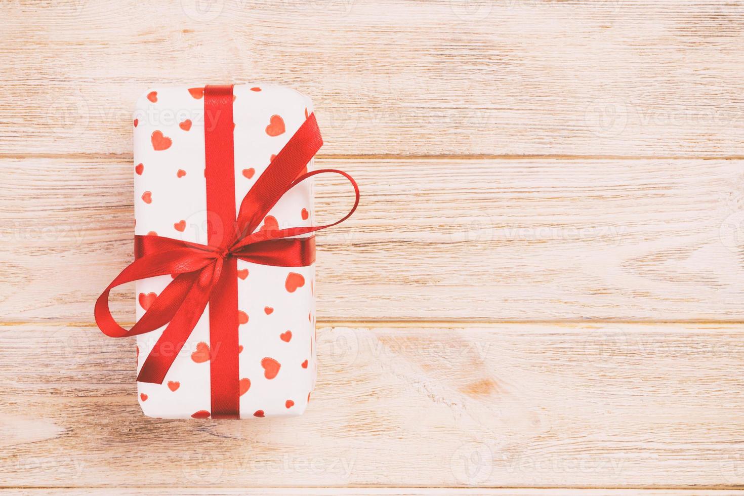Valentine or other holiday handmade present in paper with red hearts and gifts box in holiday wrapper. Present box of gift on orange wooden table top view with copy space, empty space for design photo