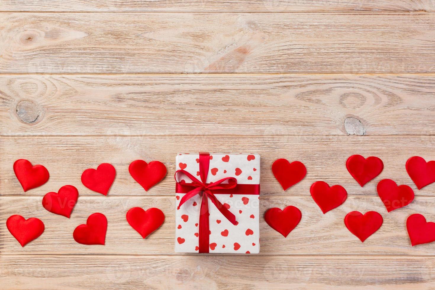 Valentine or other holiday handmade present in paper with red hearts and gifts box in holiday wrapper. Present box of gift on orange wooden table top view with copy space, empty space for design photo