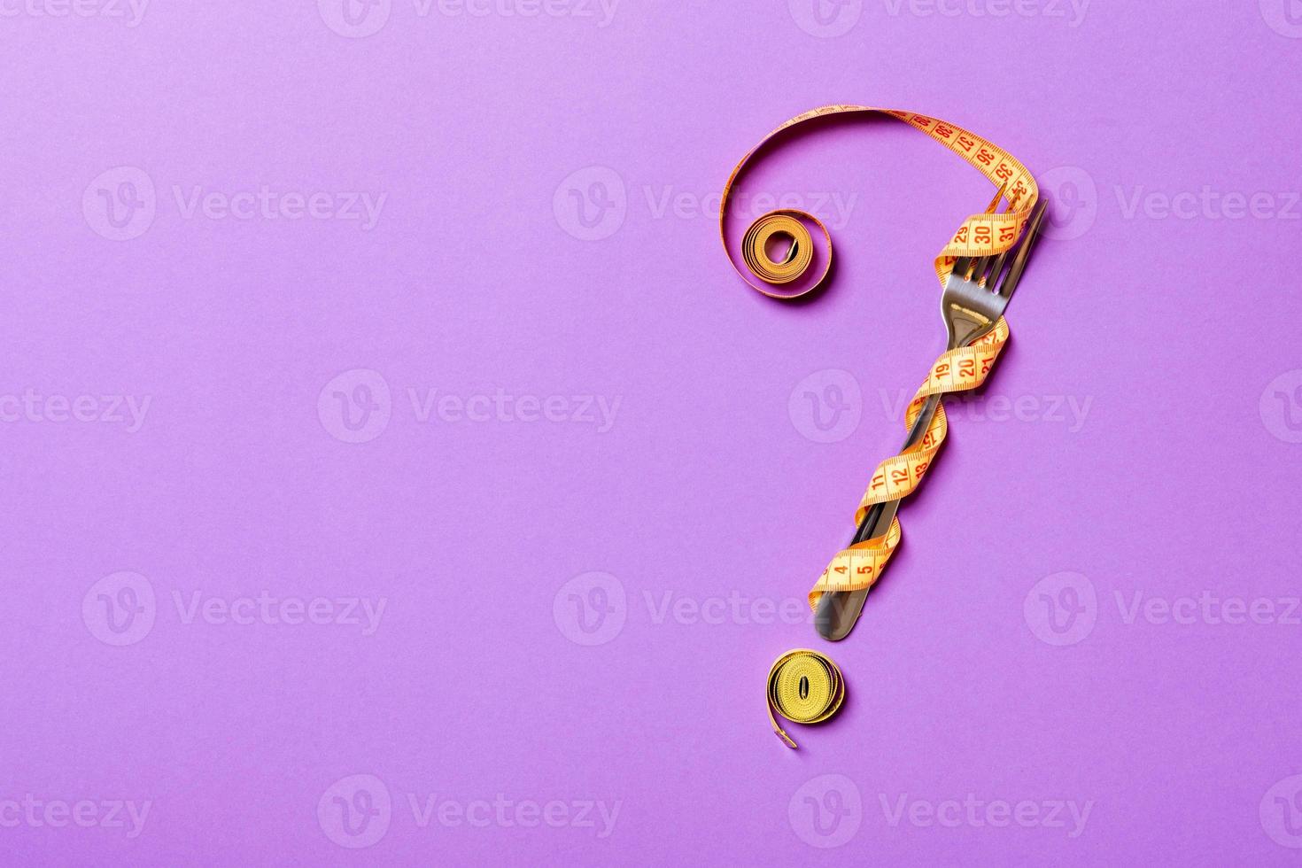 Top view of fork and measure tape in form of question mark on purple background. Overeating concept and copy space photo