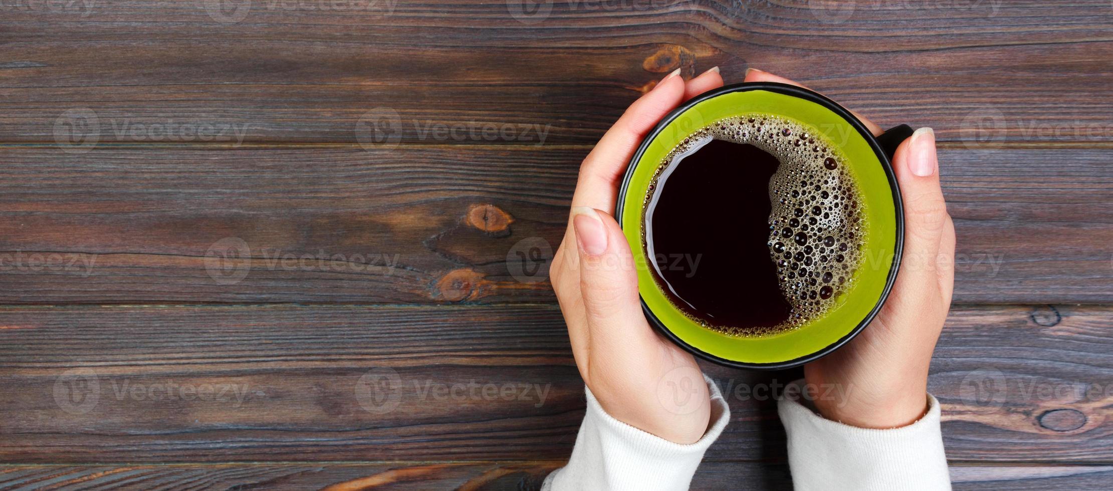 Female hands holding cup of coffee on rustic wooden table background. Banner photo