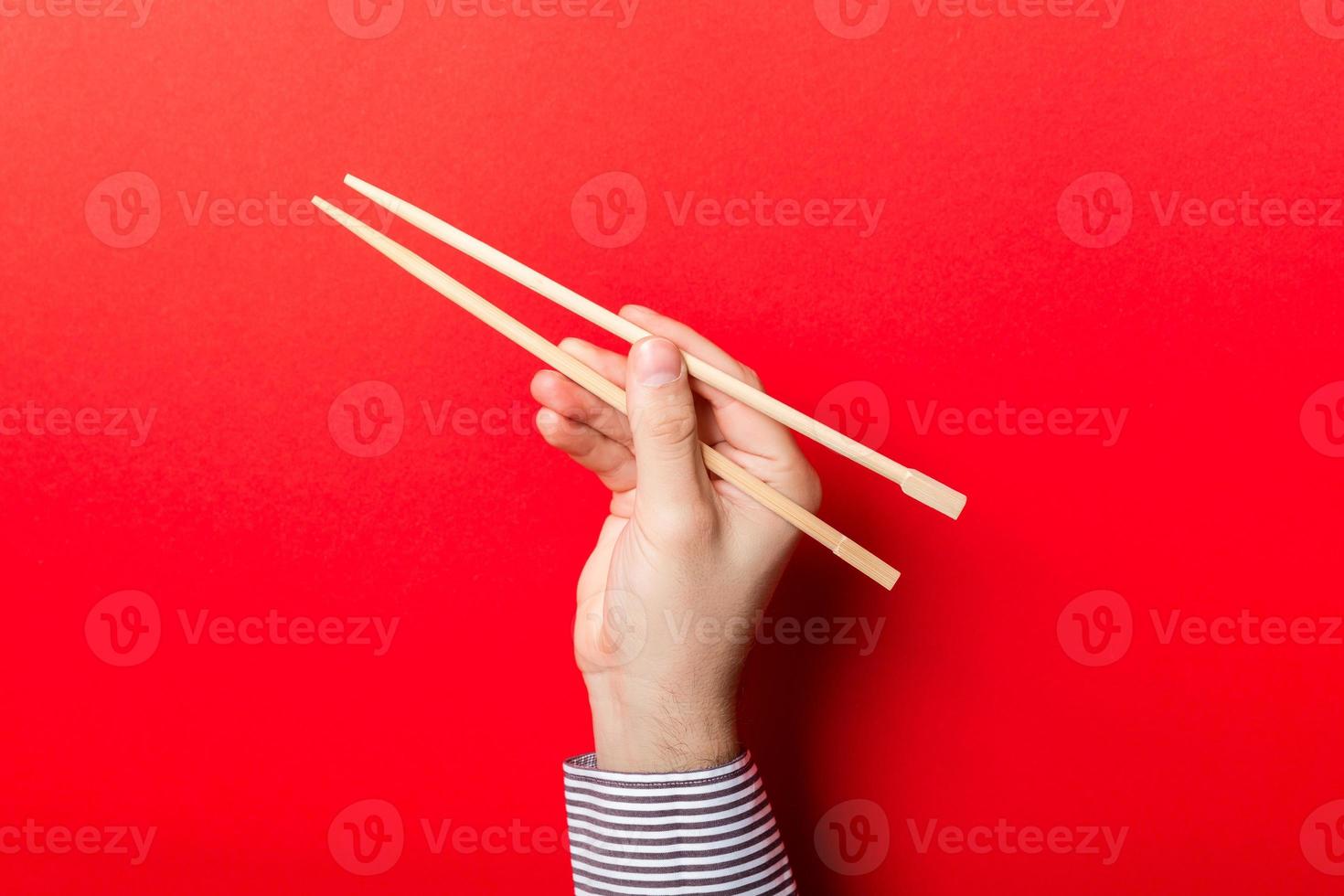 Boy's hand showing chopsticks on red background. Asian cuisine concept with empty space for your design photo