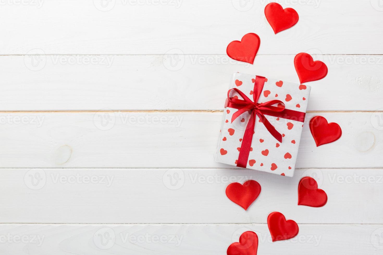 Valentine or other holiday handmade present in paper with red hearts and gifts box in holiday wrapper. Present box gift on white wooden table top view with copy space, empty space for design photo
