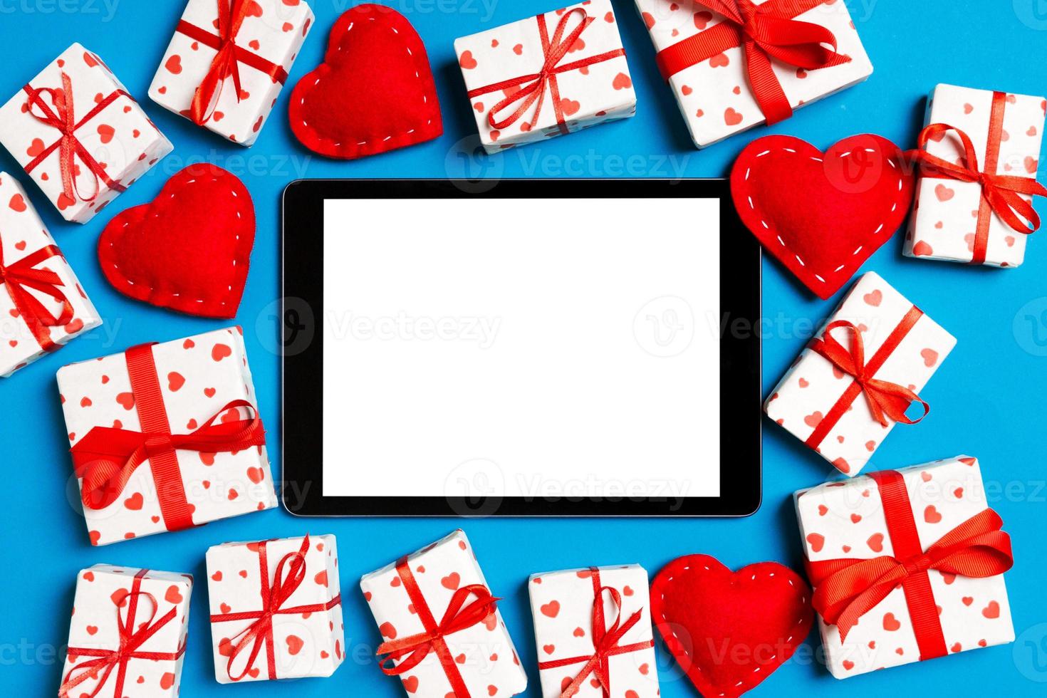 Top view of digital tablet surrounded with gift boxes and hearts on colorful background. Saint Valentine's day photo