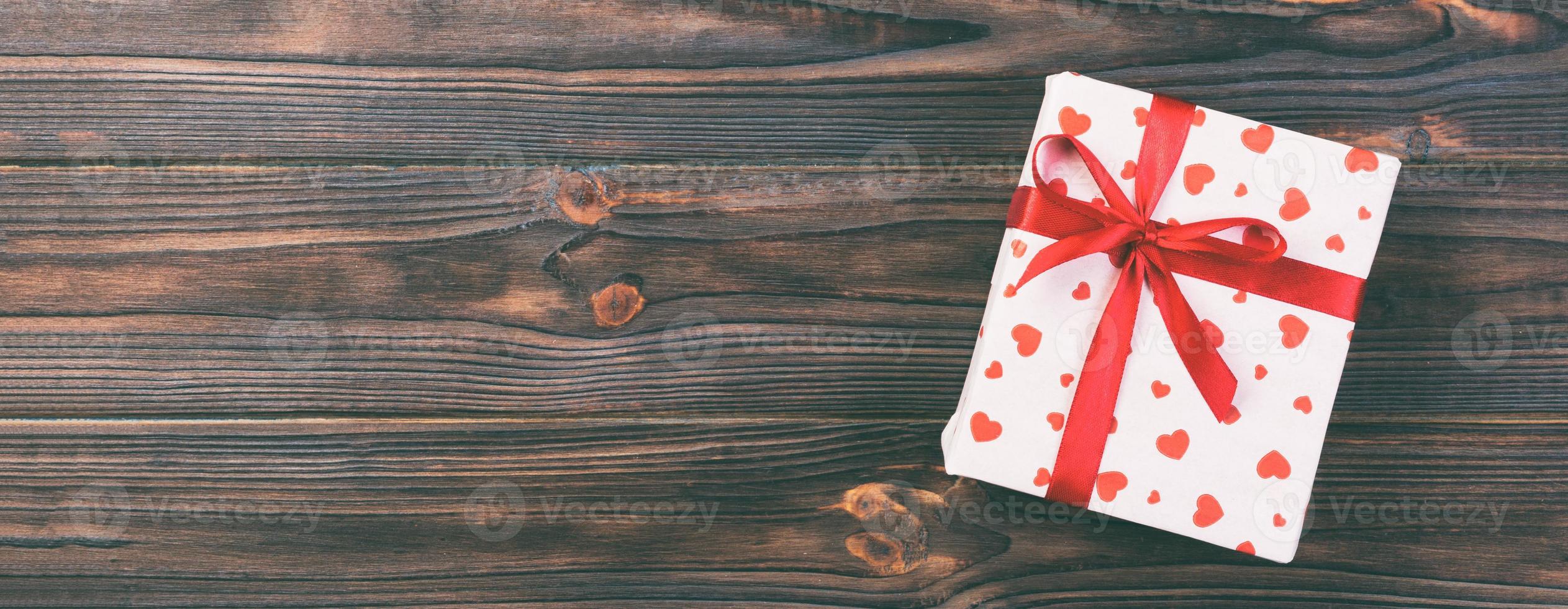 Valentine or other holiday handmade present in paper with red hearts and gifts box in holiday wrapper. Present box of gift on Dark wooden table top view with copy space, empty space for design photo