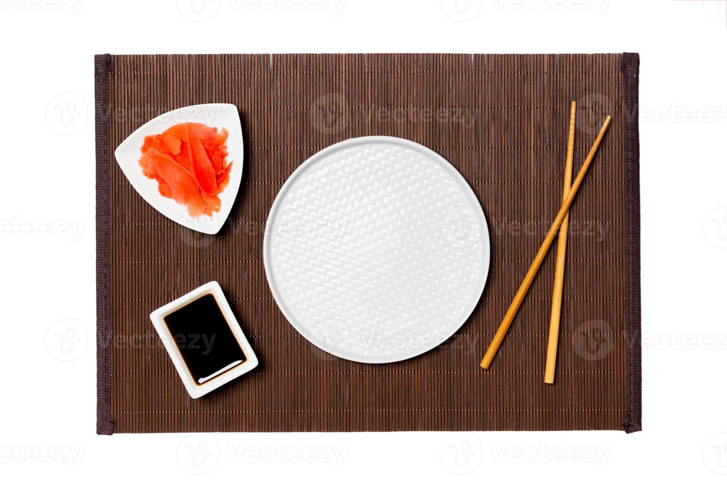 Empty round white plate with chopsticks for sushi, ginger and soy sauce on dark bamboo mat background. Top view with copy space for you design photo