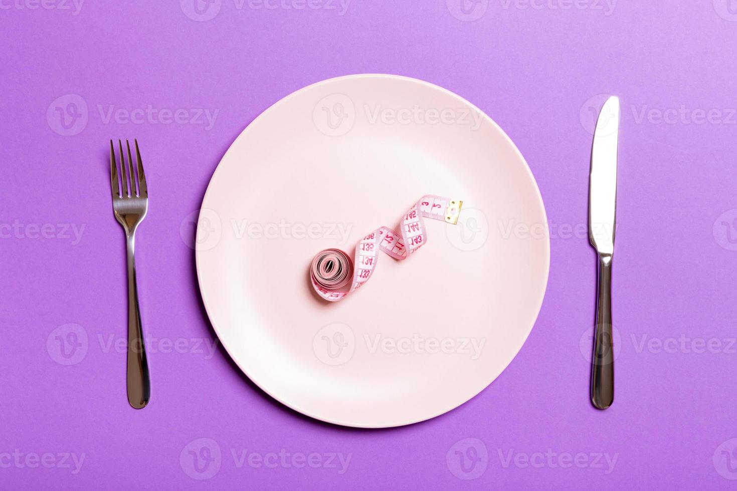 Healthy diet concept of plate with measuring tape, fork and knife on purple background. Top view photo