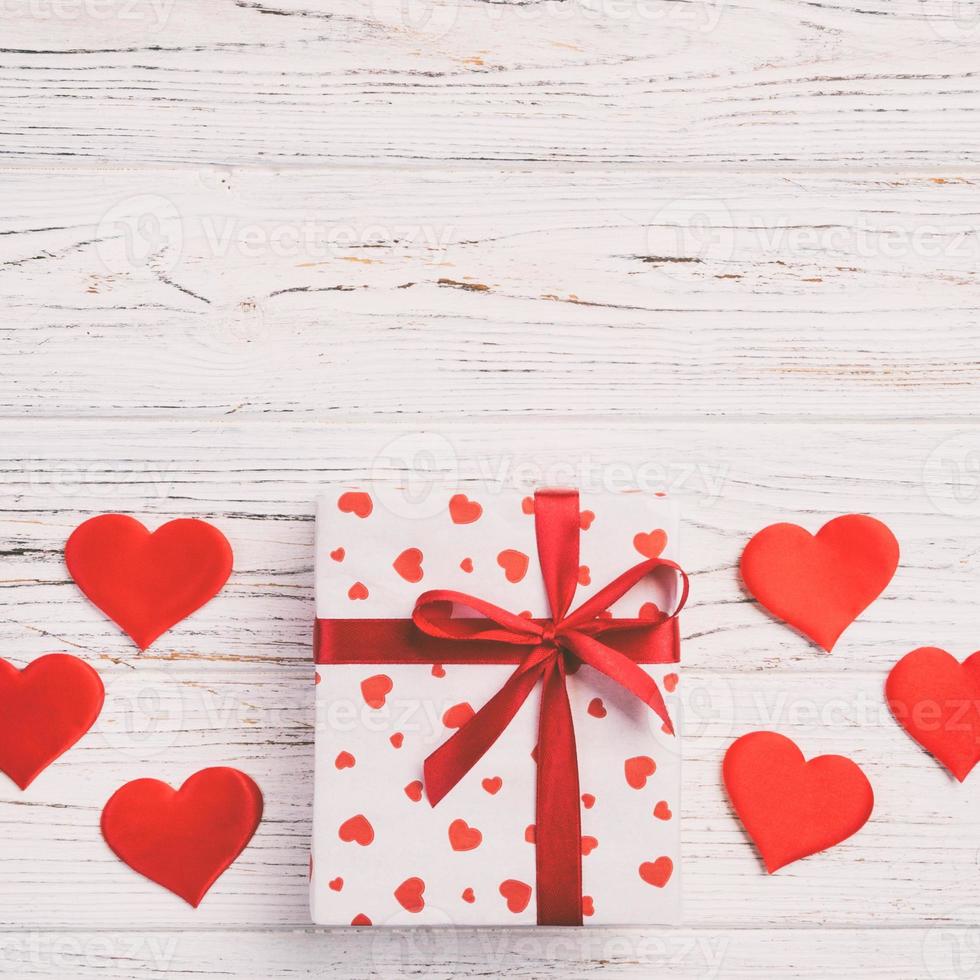 Valentine or other holiday handmade present in paper with red hearts and gifts box in holiday wrapper. Present box of gift on white wooden table top view with copy space, empty space for design photo