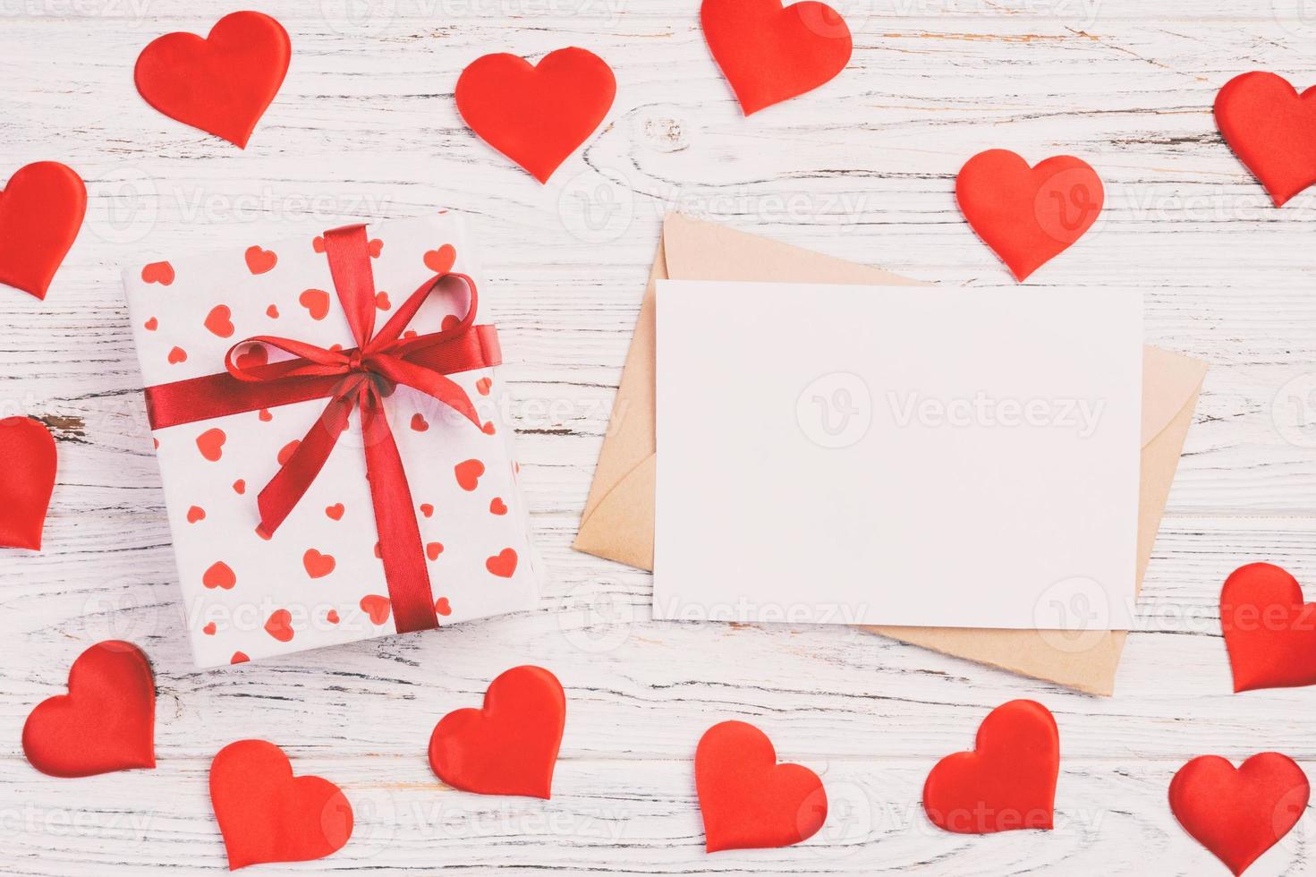 correo de sobre con corazón rojo y caja de regalo sobre fondo blanco de madera. tarjeta de san valentín, amor o concepto de saludo de boda foto