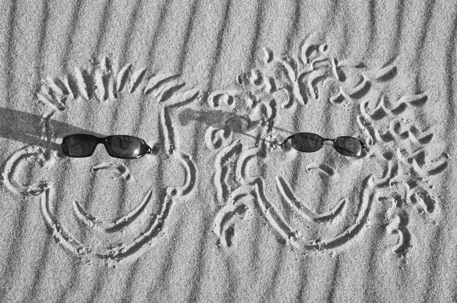 Face drawn in the sand on the beach, with sunglasses. Sand with wave pattern photo