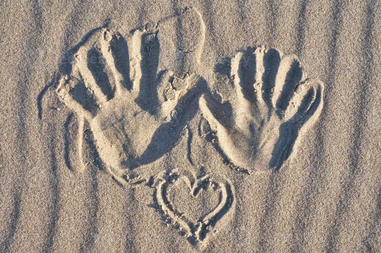 huella de mano con corazón en la arena de la playa. arena ondulada naturaleza muerta en la orilla del mar foto