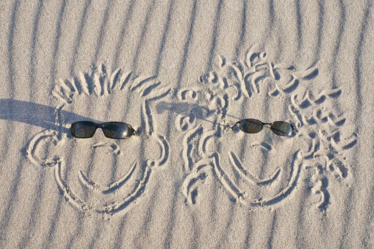 Face drawn in the sand on the beach, with sunglasses. Sand with wave pattern photo