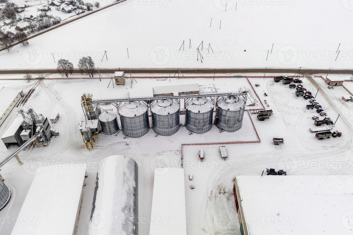 agro silos granary elevator in winter day in snowy field. Silos on agro-processing manufacturing plant for processing drying cleaning and storage of agricultural products photo