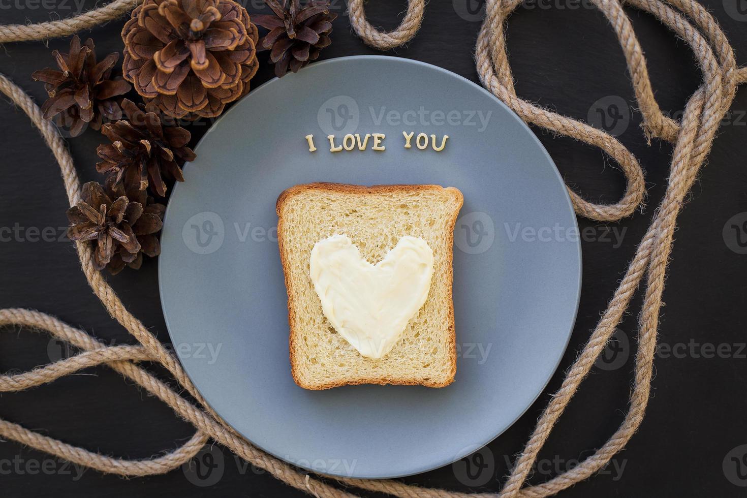 sandwich for breakfast in form of heart with cheese on a blue plate and black background with cones inscription I love you photo