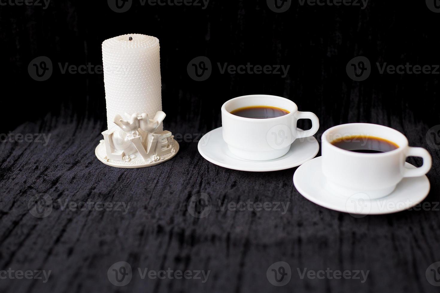 vela y dos tazas de café sobre un fondo negro foto