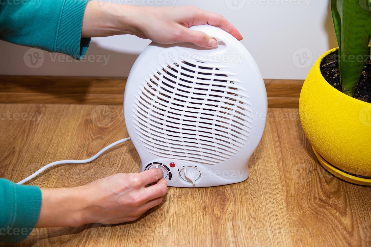 The girl holds her hands near the plastic fan heater and warms her hands, regulating the temperature at home. photo