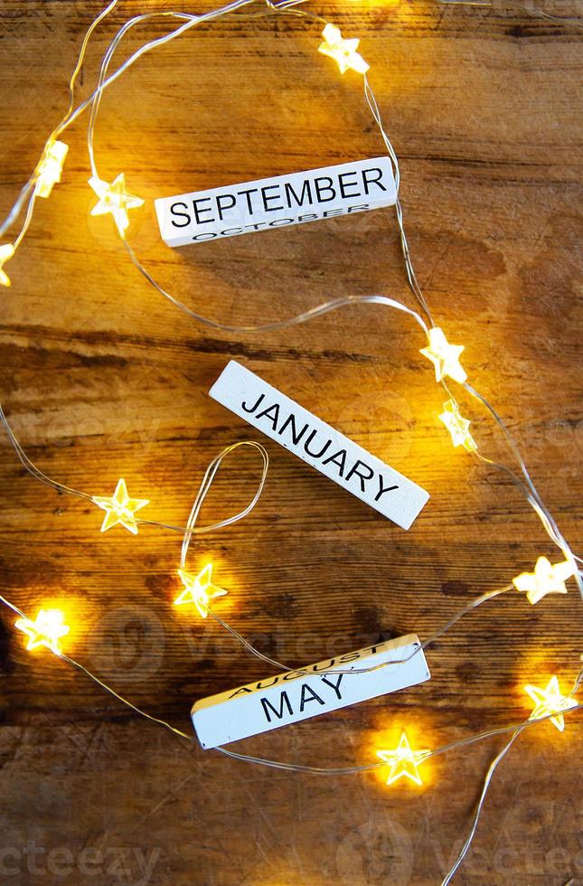 Perpetual calendar on a wooden table, different months against the background of garlands in the stars. photo