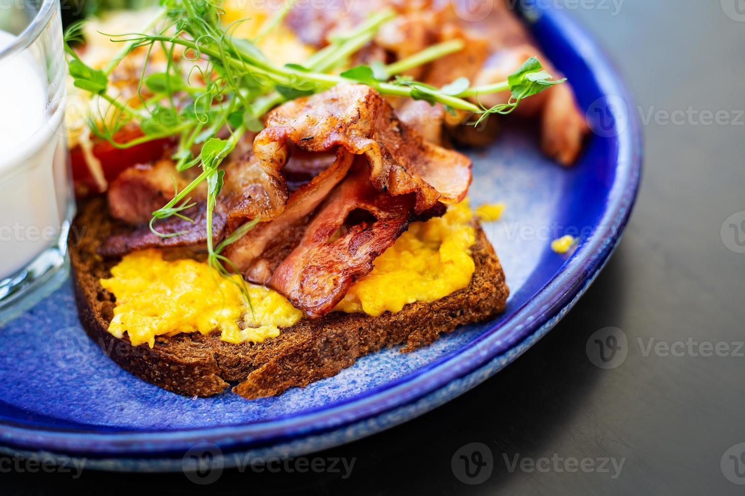desayuno muy brillante y saludable en un plato: tocino, huevo, ensalada, tomate, queso, un vaso de yogur. de cerca. foto