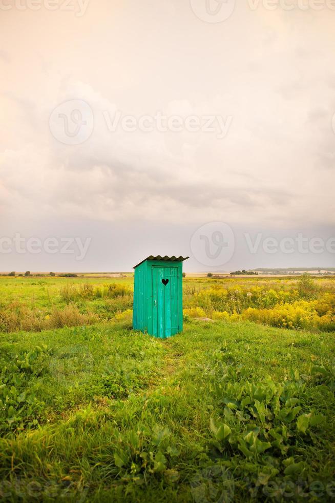 wooden toilet with a carved window in the shape of a heart, an open field photo