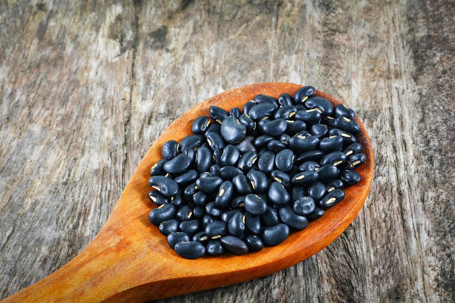 frijol negro en cuchara de madera sobre semillas de grano de fondo de madera rústica foto