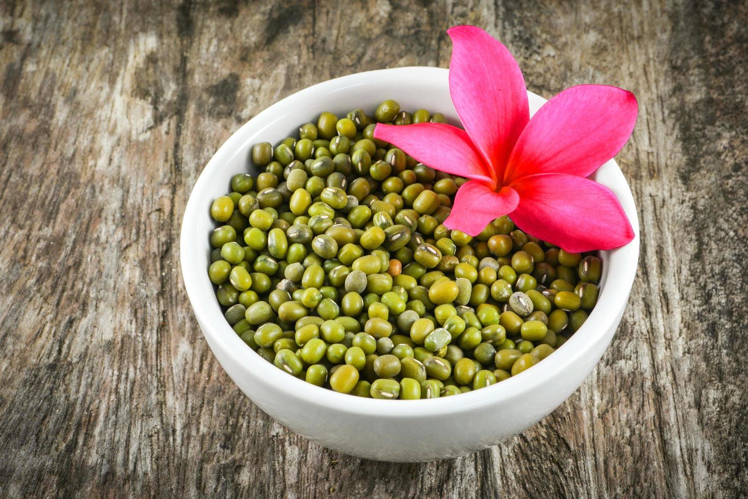 frijol mungo o semillas de judías verdes cereales integrales en tazón blanco con flor de frangipani plumeria foto