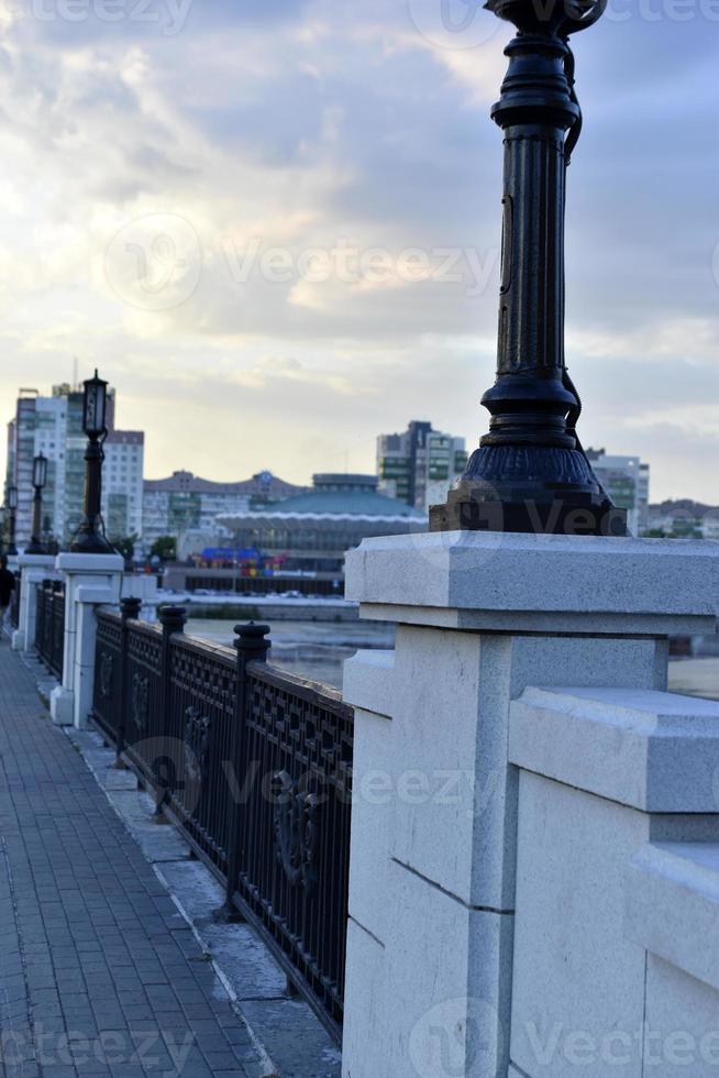 A beautiful stone bridge on the embankment in a beautiful evening. The fence of the bridge on the embankment and passers-by. photo