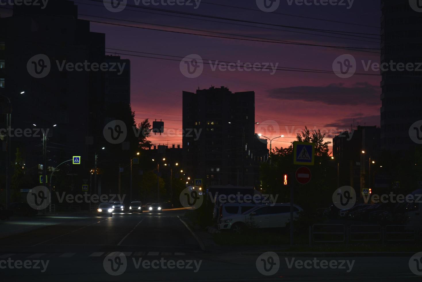 puesta de sol rosa brillante y coches en la carretera. techos de casas y una brillante puesta de sol. foto