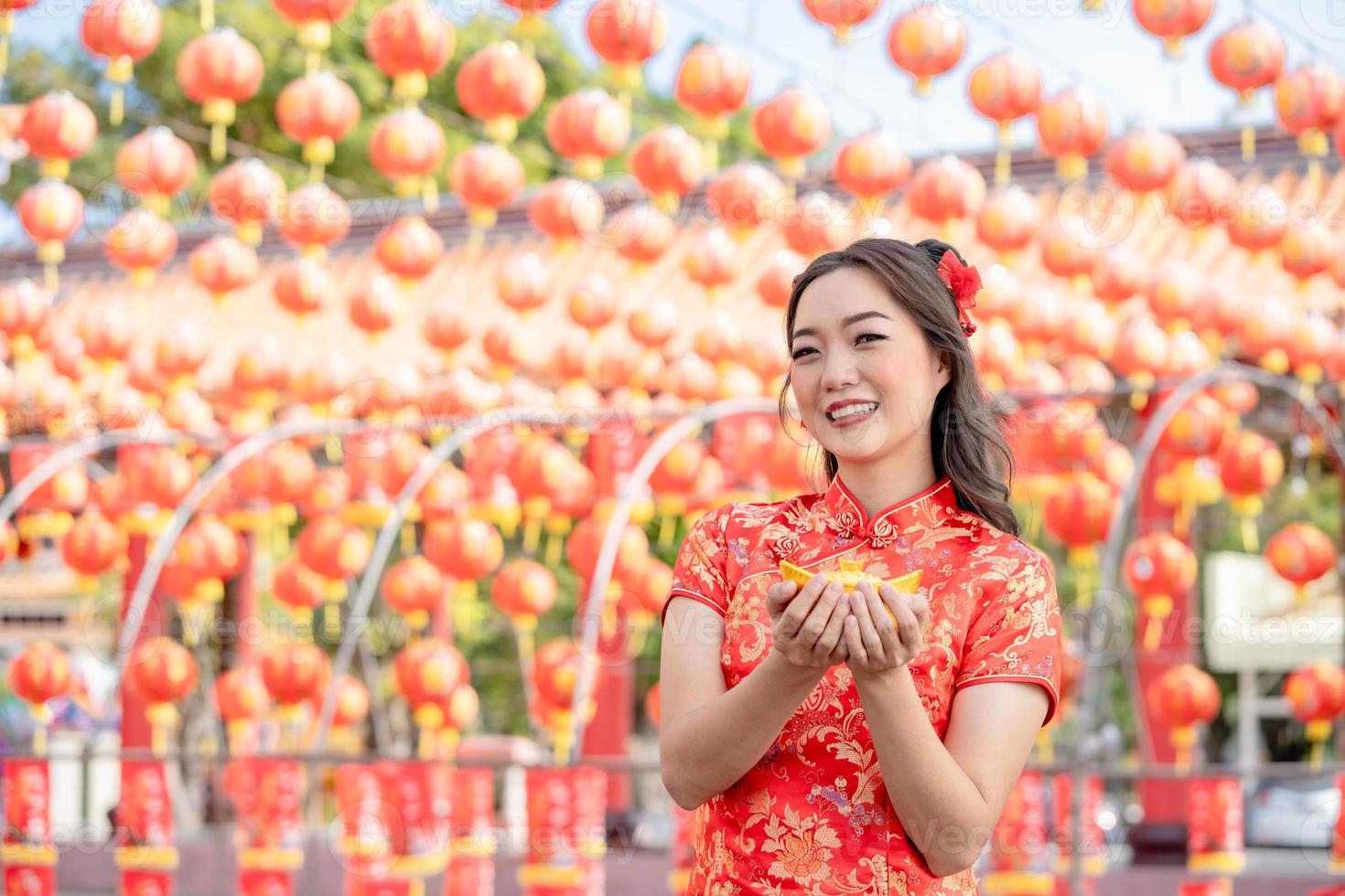 Young Asian woman wearing traditional cheongsam qipao costume holding ancient gold money in Chinese Buddhist temple. Chinese New Year concept. Emotion smile photo