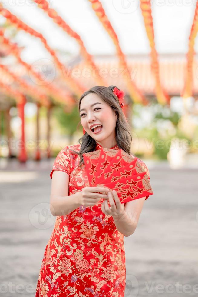 Young lady wearing traditional cheongsam qipao costume holding ang pao, red envelopes in Chinese Buddhist temple. Celebrate Chinese lunar new year, festive season holiday. photo
