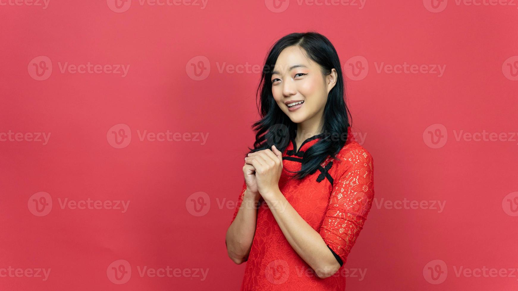 feliz año nuevo chino lunar. hermosa mujer con vestido tradicional cheongsam qipao posando orar deseo suerte aislado sobre fondo rojo. emoción sonrisa foto