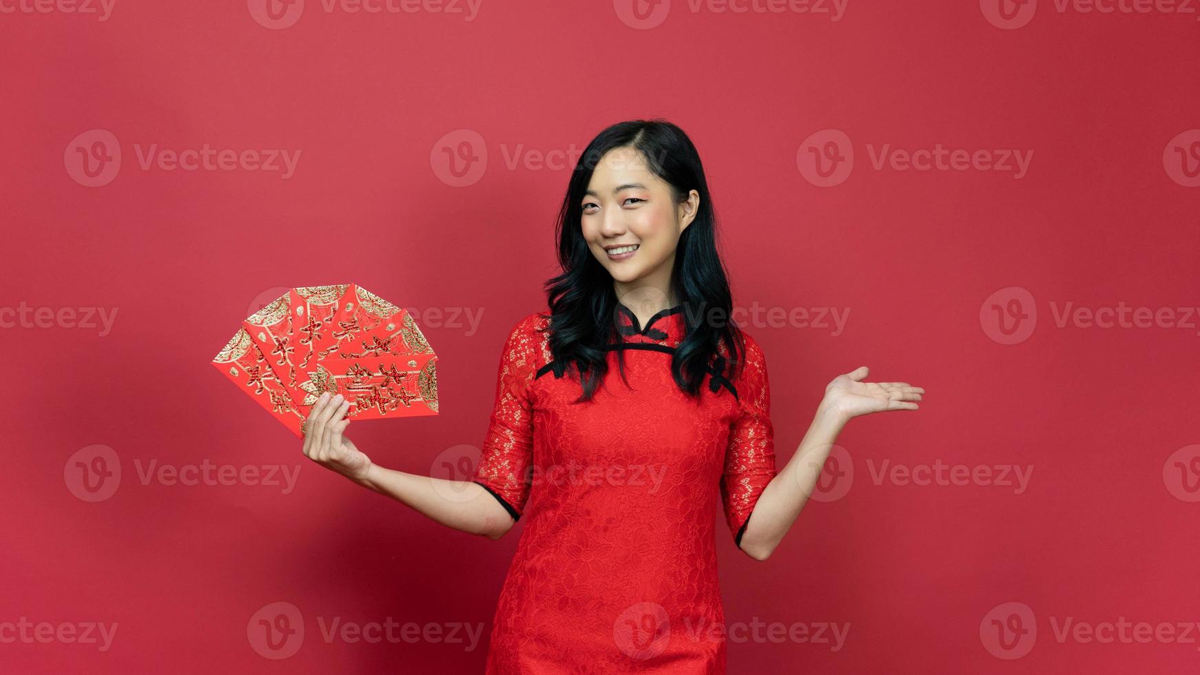 Beautiful woman wearing traditional cheongsam qipao dress holding blessing fortune card and hand present isolated on red background. Chinese text means great luck great profit photo