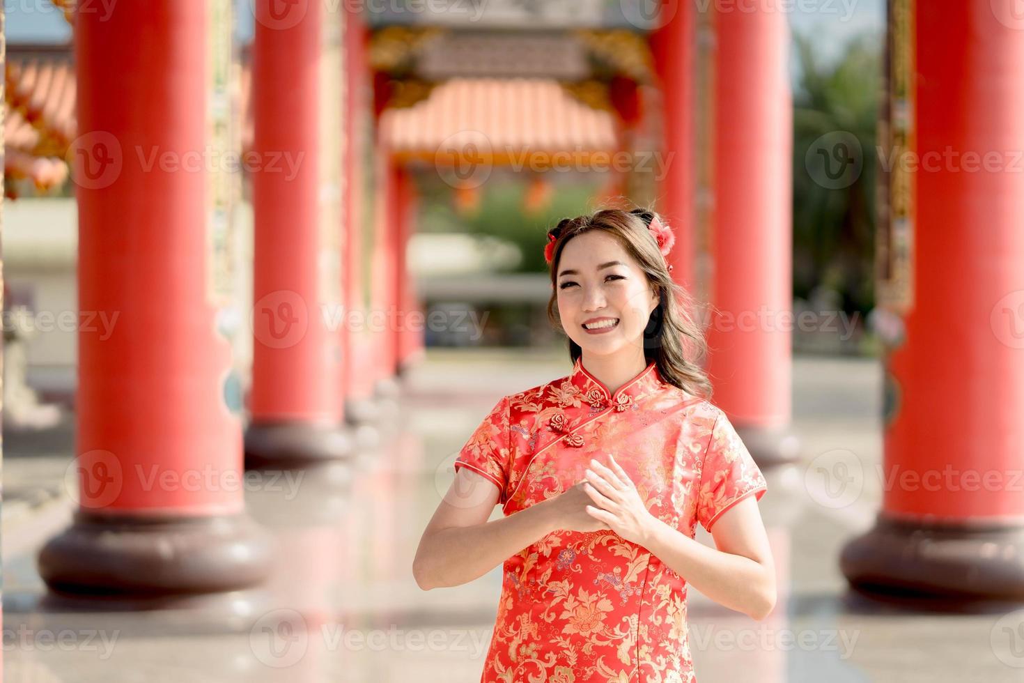 Asian woman wearing traditional cheongsam qipao dress with gesture of congratulation in Chinese Buddhist temple. Emotion smile. Chainese new year concept. Emotion Smile photo