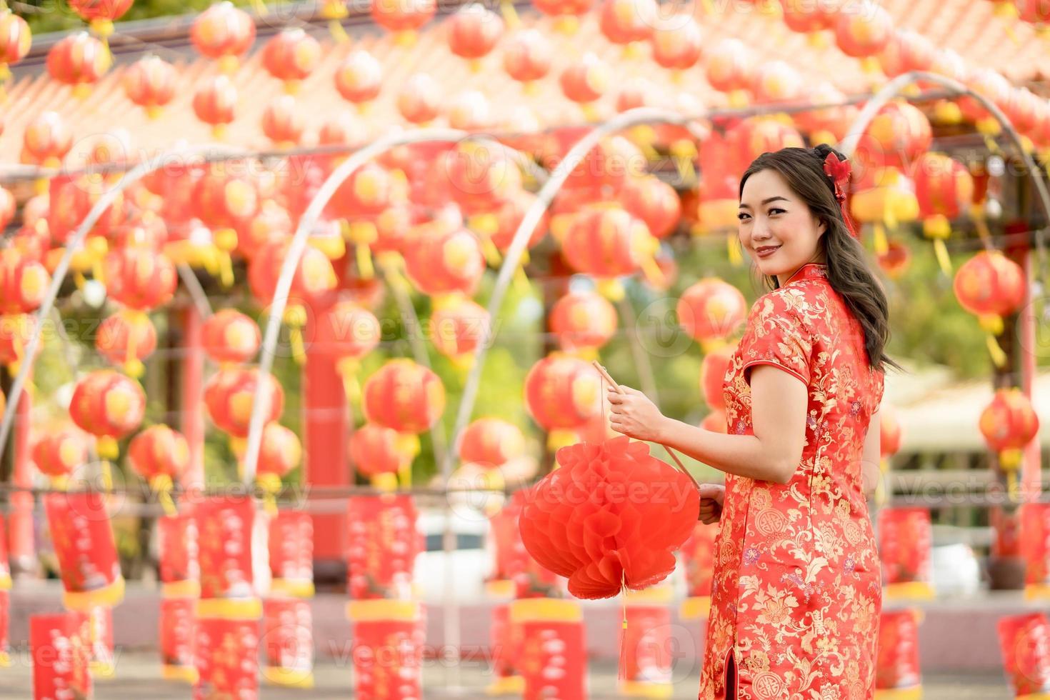 Happy Asian woman wearing traditional cheongsam qipao dress holding lantern while visiting the Chinese Buddhist temple. Celebrate Chinese lunar new year, festive season holiday. Emotion Smile photo