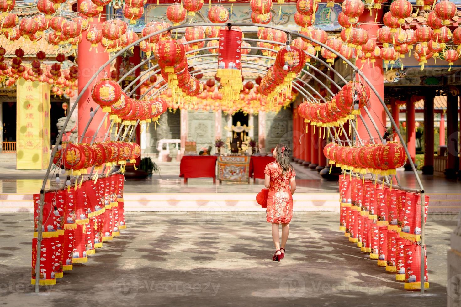 Young asian woman wearing traditional cheongsam qipao dress holding lantern and walking with her back while visiting the Chinese Buddhist temple. Celebrate Chinese lunar new year. photo