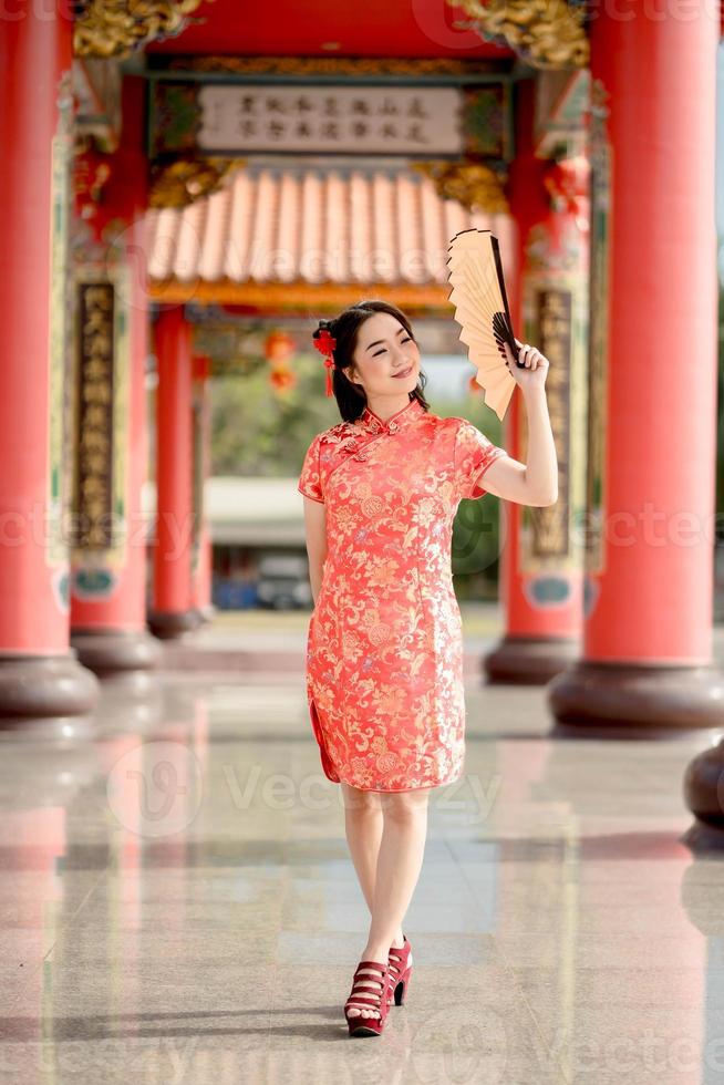 imagen vertical feliz Año Nuevo Chino. hermosa mujer asiática con vestido tradicional cheongsam qipao sosteniendo un ventilador mientras visitaba el templo budista chino foto
